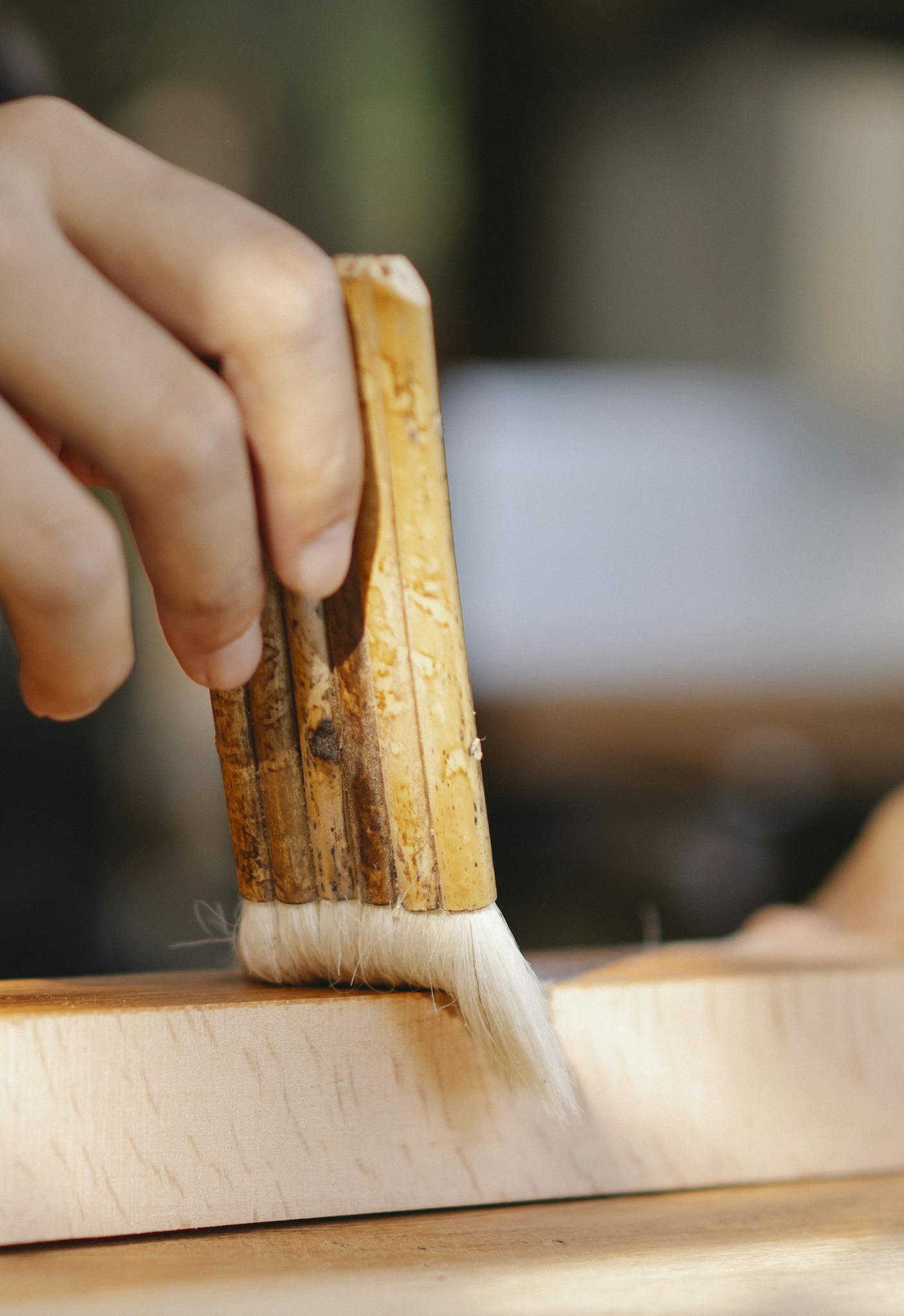 Unrecognizable craftsman applying glue on wooden board while working in joinery  on blurred background